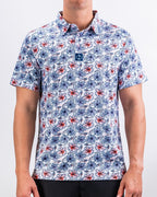 Men’s Hibiscus Harmony golf polo by Pins & Aces featuring blue and coral hibiscus flowers on a white lightweight performance golf shirt.
