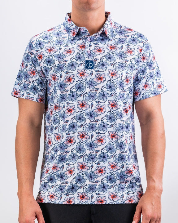 Men’s Hibiscus Harmony golf polo by Pins & Aces featuring blue and coral hibiscus flowers on a white lightweight performance golf shirt.