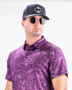 Men’s purple casino golf polo by Pins & Aces featuring an all-over pattern of playing cards, dice, poker chips, slot machines, and Las Vegas-inspired graphics.