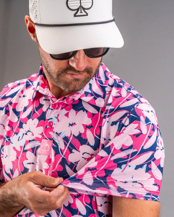 Men’s Brushed Flowers golf polo by Pins & Aces featuring a bold pink, blush, white, blue, and navy floral print with short sleeves and an athletic performance fit.
