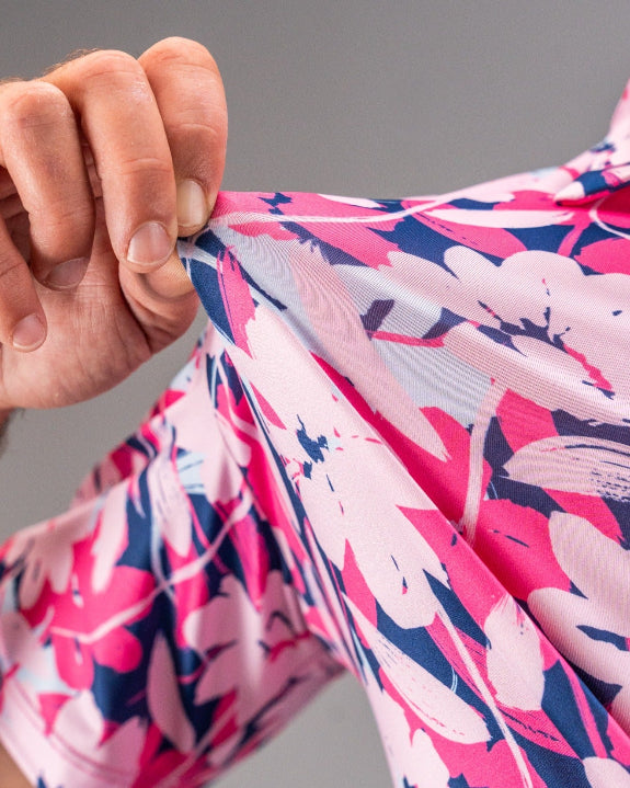 Men’s Brushed Flowers golf polo by Pins & Aces featuring a bold pink, blush, white, blue, and navy floral print with short sleeves and an athletic performance fit.