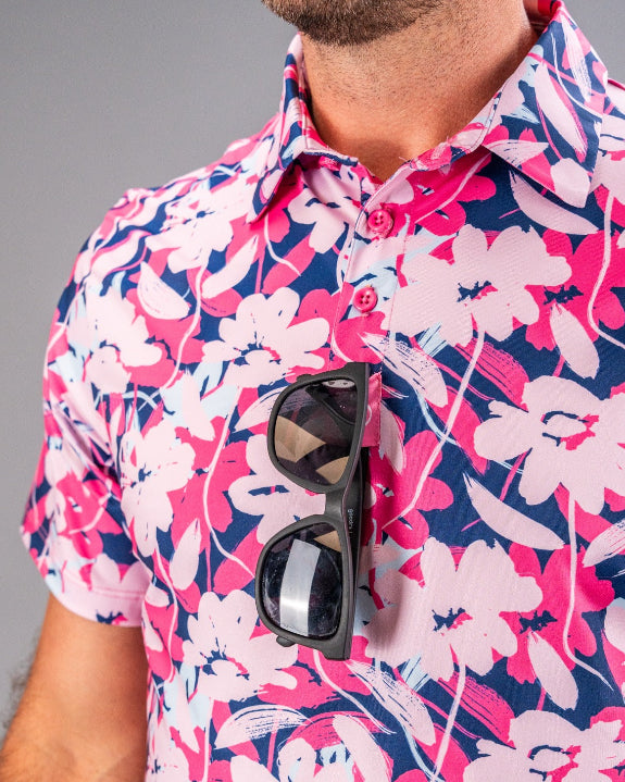 Men’s Brushed Flowers golf polo by Pins & Aces featuring a bold pink, blush, white, blue, and navy floral print with short sleeves and an athletic performance fit.