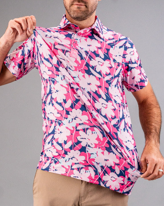 Men’s Brushed Flowers golf polo by Pins & Aces featuring a bold pink, blush, white, blue, and navy floral print with short sleeves and an athletic performance fit.