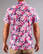 Men’s Brushed Flowers golf polo by Pins & Aces featuring a bold pink, blush, white, blue, and navy floral print with short sleeves and an athletic performance fit.