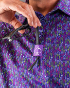 Men’s Doodle Guy Purple golf polo by Pins & Aces featuring an all-over purple, violet, blue, and green doodle-inspired pattern with short sleeves and an athletic performance fit.