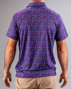 Men’s Doodle Guy Purple golf polo by Pins & Aces featuring an all-over purple, violet, blue, and green doodle-inspired pattern with short sleeves and an athletic performance fit.