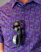 Men’s Doodle Guy Purple golf polo by Pins & Aces featuring an all-over purple, violet, blue, and green doodle-inspired pattern with short sleeves and an athletic performance fit.