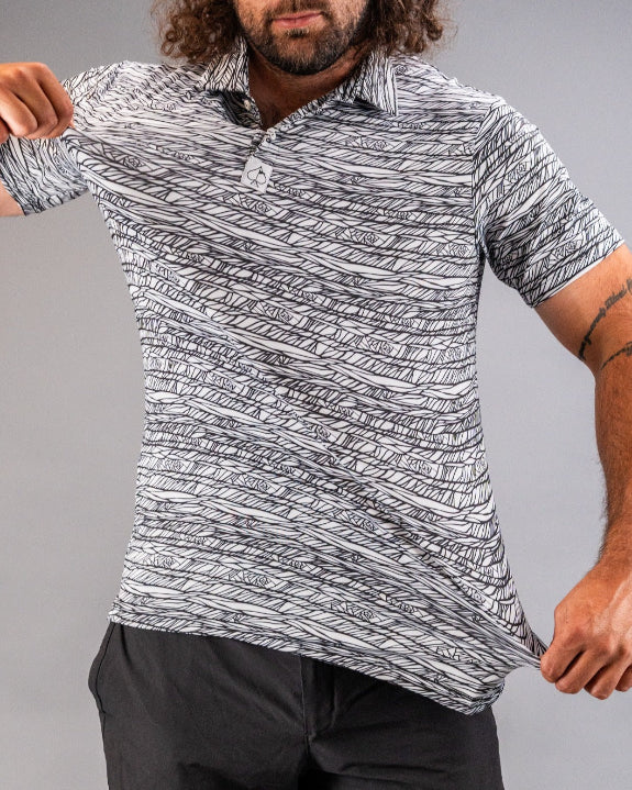 Men’s Fragment Black golf polo by Pins & Aces featuring an all-over black, white, and gray abstract line pattern with short sleeves and an athletic performance fit.