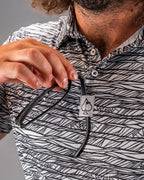 Men’s Fragment Black golf polo by Pins & Aces featuring an all-over black, white, and gray abstract line pattern with short sleeves and an athletic performance fit.