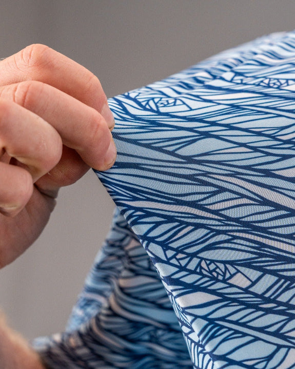 Men’s Fragment Blue golf polo by Pins & Aces featuring an all-over abstract fragmented line pattern in blue and white with short sleeves and an athletic performance fit.