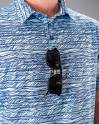 Men’s Fragment Blue golf polo by Pins & Aces featuring an all-over abstract fragmented line pattern in blue and white with short sleeves and an athletic performance fit.