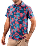 Men’s Painted Monstera Blue golf polo by Pins & Aces featuring coral and aqua tropical monstera leaves on a deep blue background with short sleeves and an athletic performance fit.