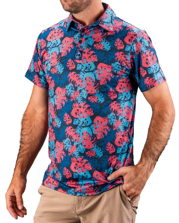 Men’s Painted Monstera Blue golf polo by Pins & Aces featuring coral and aqua tropical monstera leaves on a deep blue background with short sleeves and an athletic performance fit.