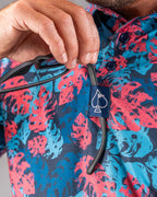 Men’s Painted Monstera Blue golf polo by Pins & Aces featuring coral and aqua tropical monstera leaves on a deep blue background with short sleeves and an athletic performance fit.
