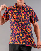 Men’s Palm Drip Dusk golf polo by Pins & Aces featuring navy palm tree silhouettes over a vibrant orange, pink, and purple tropical sunset print with an athletic fit.