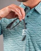 Men’s Squiggle Teal golf polo by Pins & Aces featuring an all-over aqua and teal abstract wavy squiggle pattern with short sleeves and an athletic performance fit.