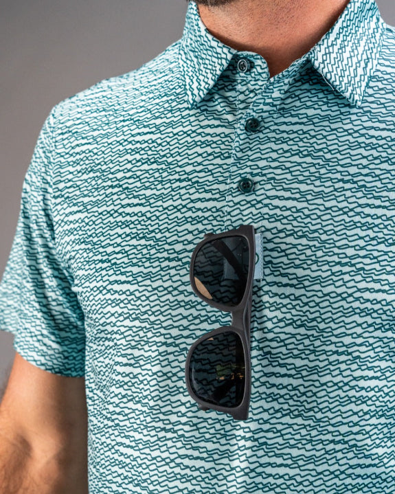Men’s Squiggle Teal golf polo by Pins & Aces featuring an all-over aqua and teal abstract wavy squiggle pattern with short sleeves and an athletic performance fit.