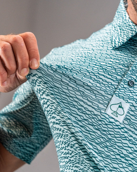 Men’s Squiggle Teal golf polo by Pins & Aces featuring an all-over aqua and teal abstract wavy squiggle pattern with short sleeves and an athletic performance fit.