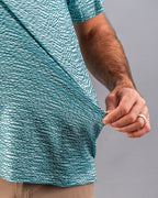 Men’s Squiggle Teal golf polo by Pins & Aces featuring an all-over aqua and teal abstract wavy squiggle pattern with short sleeves and an athletic performance fit.