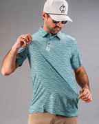 Men’s Squiggle Teal golf polo by Pins & Aces featuring an all-over aqua and teal abstract wavy squiggle pattern with short sleeves and an athletic performance fit.