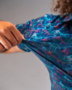 Men’s Swordfish Skelly golf polo by Pins & Aces featuring a blue, teal, and red ocean-inspired swordfish pattern with short sleeves and an athletic performance fit.