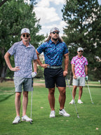 Men’s Swordfish Skelly golf polo by Pins & Aces featuring a blue, teal, and red ocean-inspired swordfish pattern with short sleeves and an athletic performance fit.