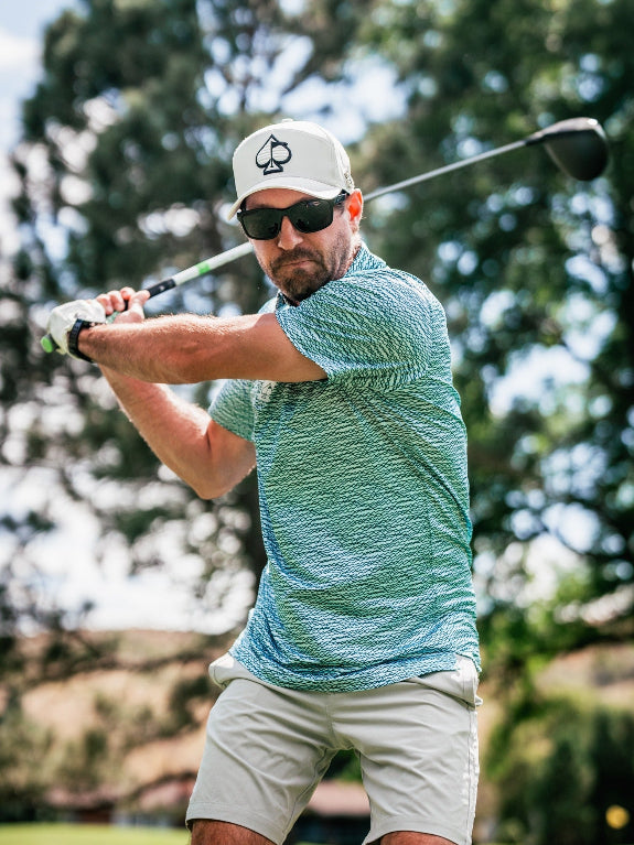 Men’s Squiggle Teal golf polo by Pins & Aces featuring an all-over aqua and teal abstract wavy squiggle pattern with short sleeves and an athletic performance fit.