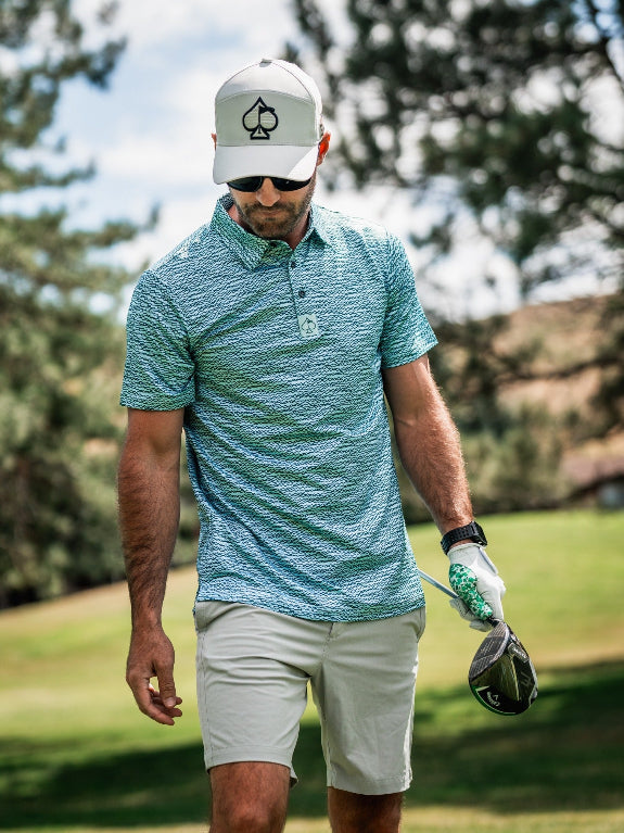 Men’s Squiggle Teal golf polo by Pins & Aces featuring an all-over aqua and teal abstract wavy squiggle pattern with short sleeves and an athletic performance fit.