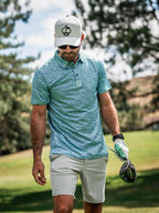 Men’s Squiggle Teal golf polo by Pins & Aces featuring an all-over aqua and teal abstract wavy squiggle pattern with short sleeves and an athletic performance fit.
