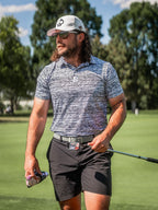 Men’s Fragment Black golf polo by Pins & Aces featuring an all-over black, white, and gray abstract line pattern with short sleeves and an athletic performance fit.