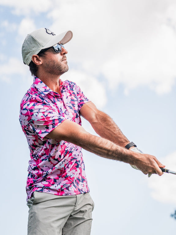 Men’s Brushed Flowers golf polo by Pins & Aces featuring a bold pink, blush, white, blue, and navy floral print with short sleeves and an athletic performance fit.