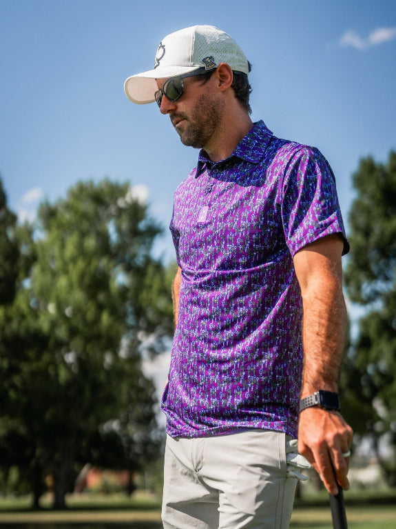 Men’s Doodle Guy Purple golf polo by Pins & Aces featuring an all-over purple, violet, blue, and green doodle-inspired pattern with short sleeves and an athletic performance fit.