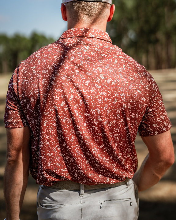 Men’s Autumn Bloom golf polo by Pins & Aces featuring a rust-colored all-over cream floral print, short sleeves, blade collar, and athletic performance fit.