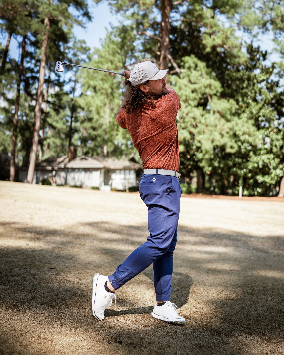 Men’s Filament golf polo by Pins & Aces featuring a rust and burnt orange abstract line pattern, short sleeves, modern blade collar, and athletic performance fit.