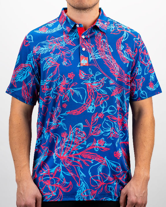 Men’s Cabo Colada golf polo by Pins & Aces featuring a vibrant coral red and aqua tropical floral print on a rich blue background with short sleeves and an athletic performance fit.