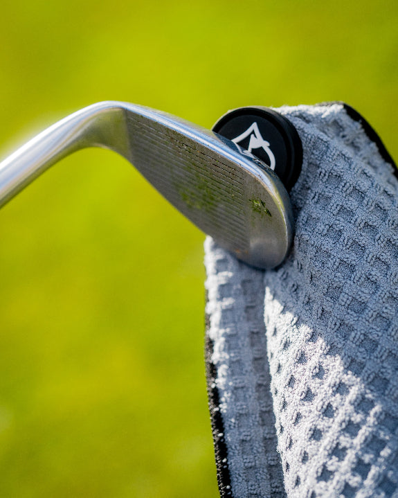 White Pins & Aces magnetic golf towel featuring durable waffle-knit fabric, a strong built-in magnet, center slit, and carabiner for attaching to a golf bag.