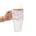 Clear glass cup with bamboo lid and straw featuring a pink pastel bookish collage with books, flowers, reading glasses, hearts and feminine reader-themed sayings.
