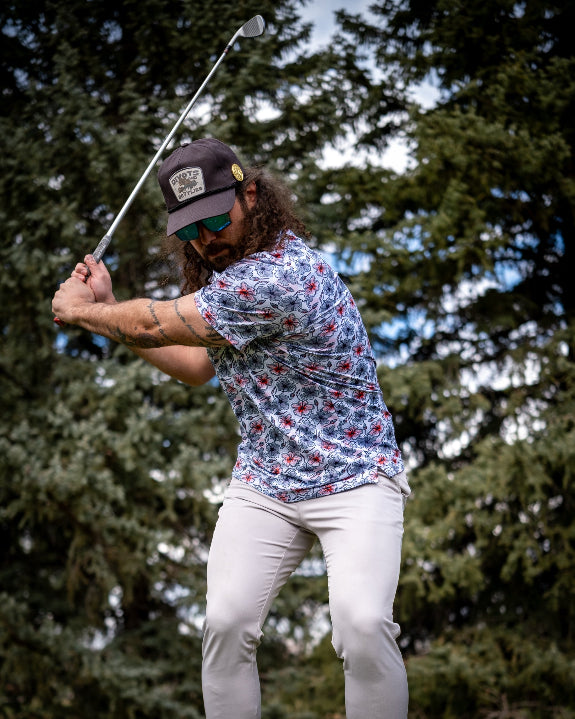 Men’s Hibiscus Harmony golf polo by Pins & Aces featuring blue and coral hibiscus flowers on a white lightweight performance golf shirt.