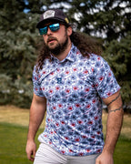 Men’s Hibiscus Harmony golf polo by Pins & Aces featuring blue and coral hibiscus flowers on a white lightweight performance golf shirt.
