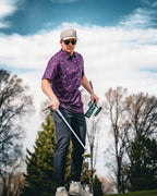 Men’s purple casino golf polo by Pins & Aces featuring an all-over pattern of playing cards, dice, poker chips, slot machines, and Las Vegas-inspired graphics.