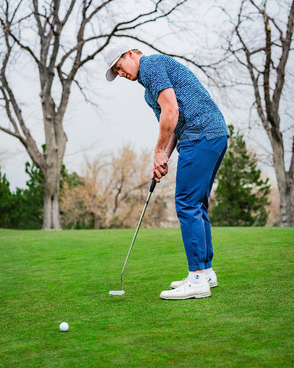 Men’s Rising Tides golf polo by Pins & Aces featuring a repeating blue and navy wave-inspired pattern, short sleeves, and an athletic performance fit.