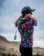 Men’s Cabo Electric golf polo by Pins & Aces featuring an aqua, hot pink, and coral tropical floral and leaf print on a dark charcoal background with an athletic performance fit.
