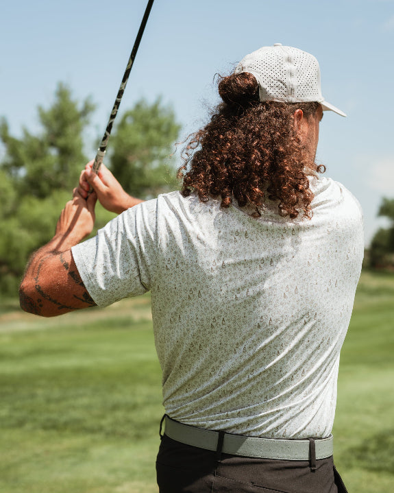 Men’s Drinking Buddies golf polo by Pins & Aces featuring a subtle drinking-inspired all-over print on a cream short-sleeve performance polo with an athletic fit.