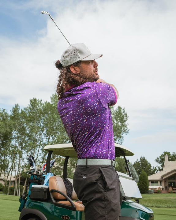 Men’s Eighties Arcade golf polo by Pins & Aces featuring a purple retro geometric print with pink and teal accents, short sleeves, and an athletic performance fit.