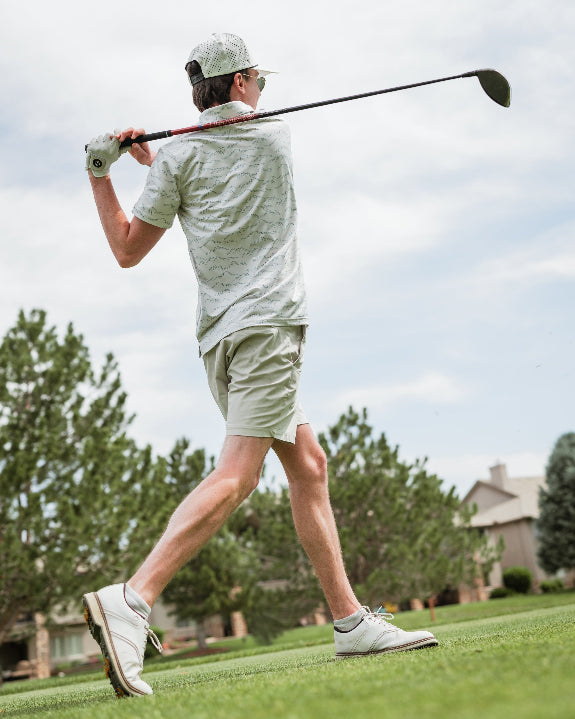 Men’s Altitude Adjustment golf polo by Pins & Aces featuring an off-white base with a subtle blue-green mountain range print, short sleeves, and athletic performance fit.