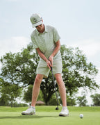 Men’s Altitude Adjustment golf polo by Pins & Aces featuring an off-white base with a subtle blue-green mountain range print, short sleeves, and athletic performance fit.