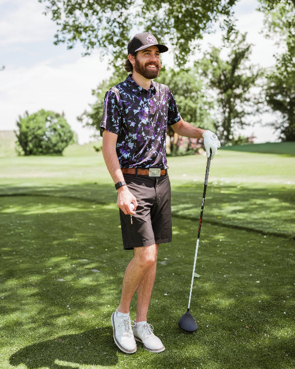 Men’s Moon Burn golf polo by Pins & Aces featuring an abstract purple, blue, and black cosmic-inspired pattern with short sleeves and an athletic performance fit.