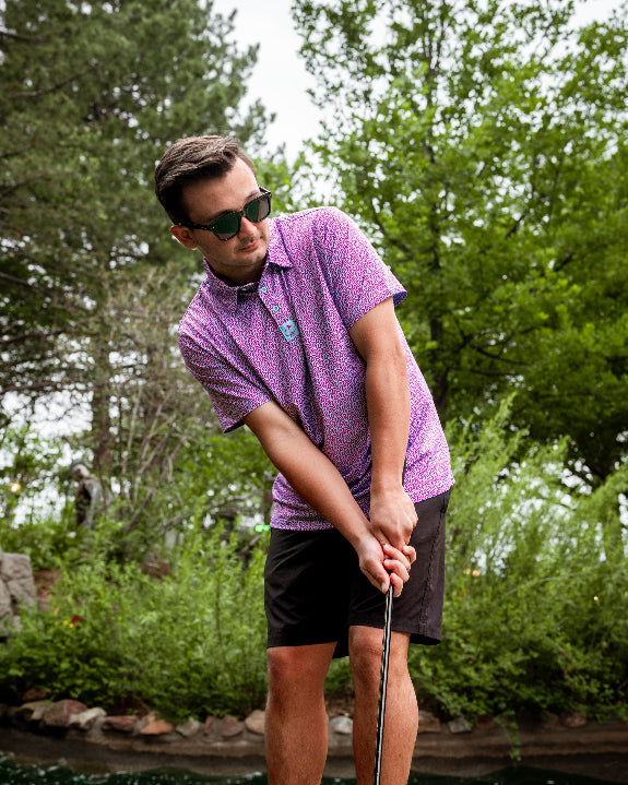 Men’s Sugar Circuit golf polo by Pins & Aces featuring a vibrant pink, purple, and blue geometric all-over pattern with short sleeves and an athletic performance fit.