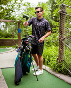 Men’s Shadow Ops black camo golf polo by Pins & Aces featuring a tonal black and charcoal camouflage pattern, short sleeves, collared neckline, and athletic fit.