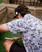 Men’s Arctic Ops golf polo by Pins & Aces featuring an all-over gray, silver, and black camouflage print with short sleeves, collared neckline, and athletic performance fit.